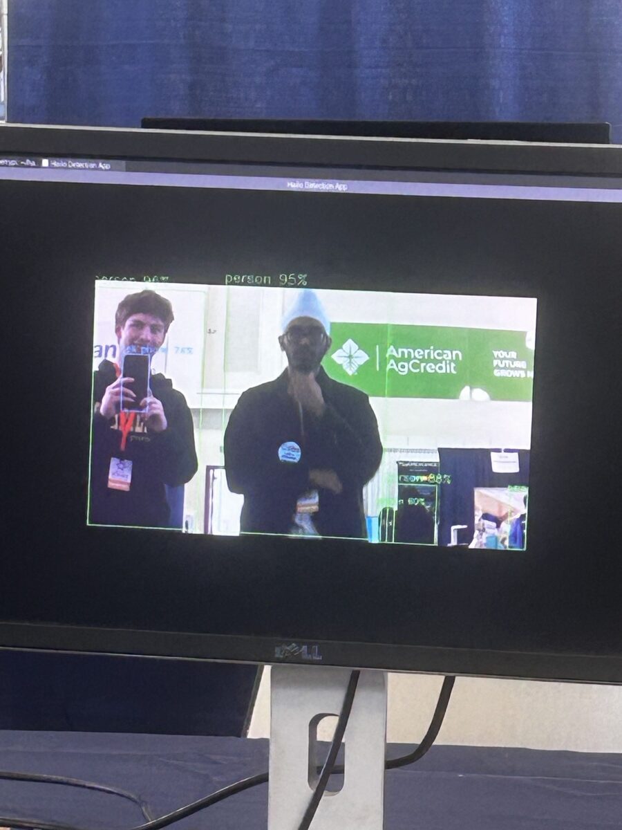 Monitor showing the detection app drawing boxes around people with confidence scores